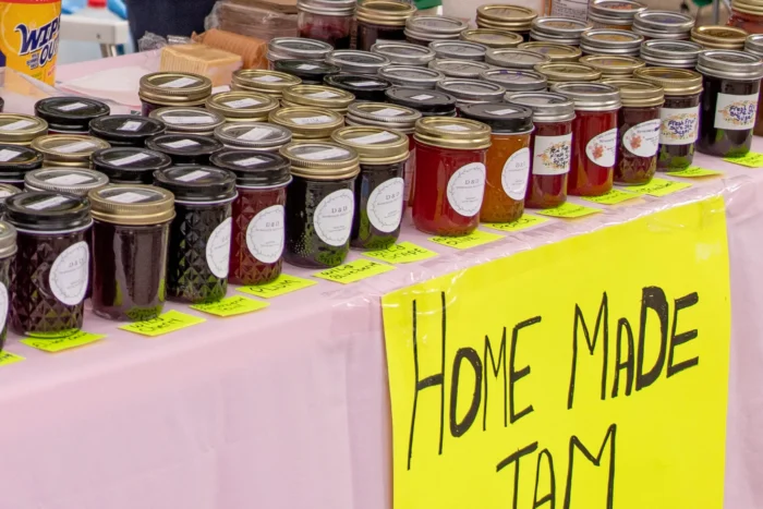 Rows of homemade jam and preserve jars with yellow "Home Made Jam" sign at farmers market stand