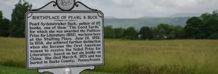 Historical marker sign designating the birthplace of Pearl S. Buck, set against a grassy field with rolling mountains in the background.