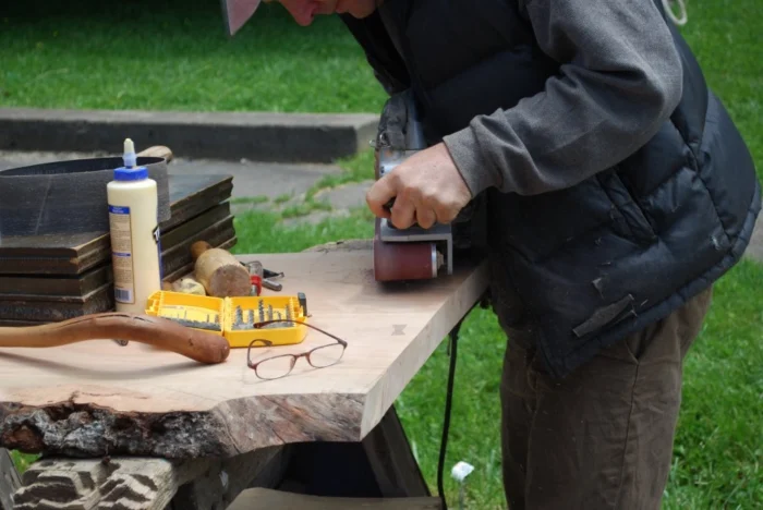 Person using power sander on wooden board at outdoor workbench