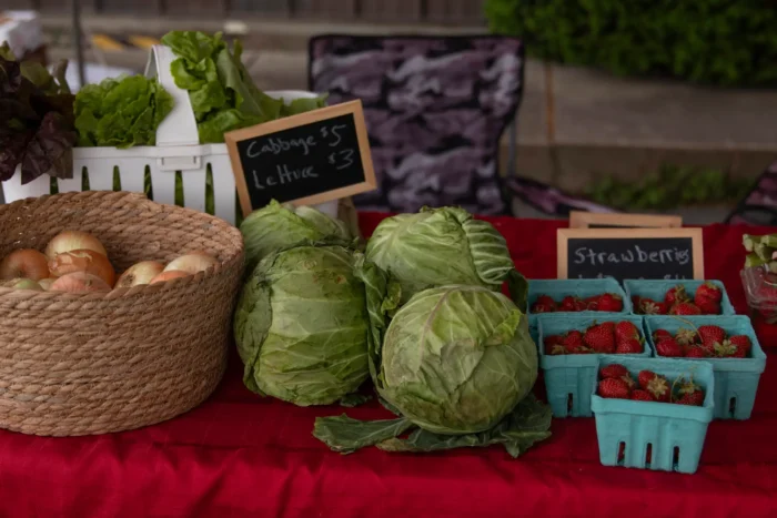 Close-up of a farmers market table displaying fresh produce including cabbages, onions, and strawberries in baskets and cartons.