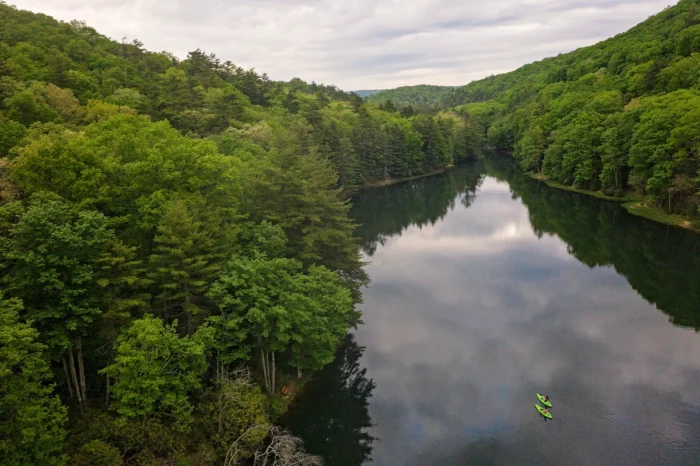 Aerial view of a lake surrounded by forested hills, with two small kayaks visible on the water.
