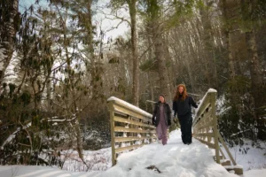 Two people walking across a snow-covered wooden bridge in winter