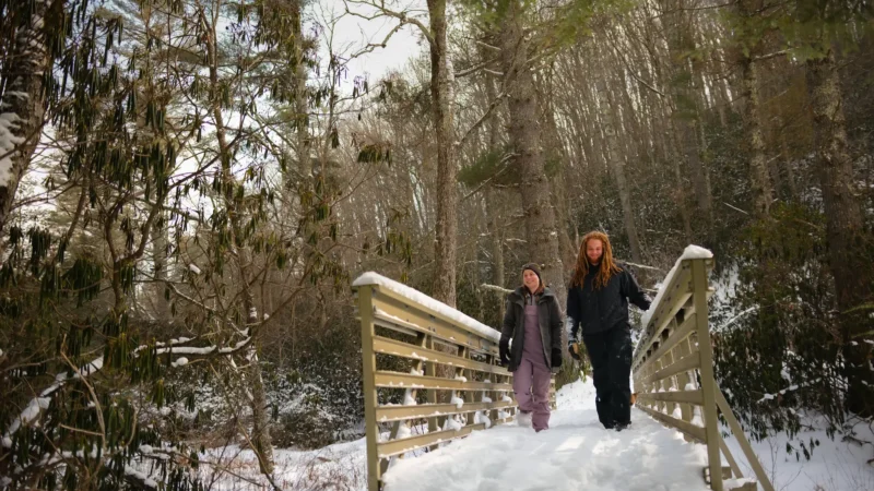 Two people walking across a snow-covered wooden bridge in winter
