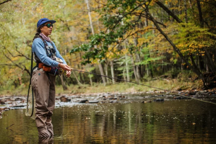 Person fly fishing in a shallow autumn river surrounded by colorful fall foliage