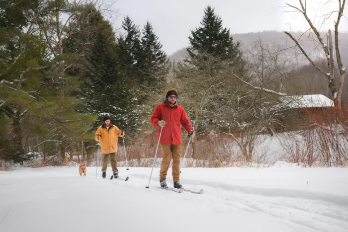 Two people cross-country skiing with a dog on a snowy trail