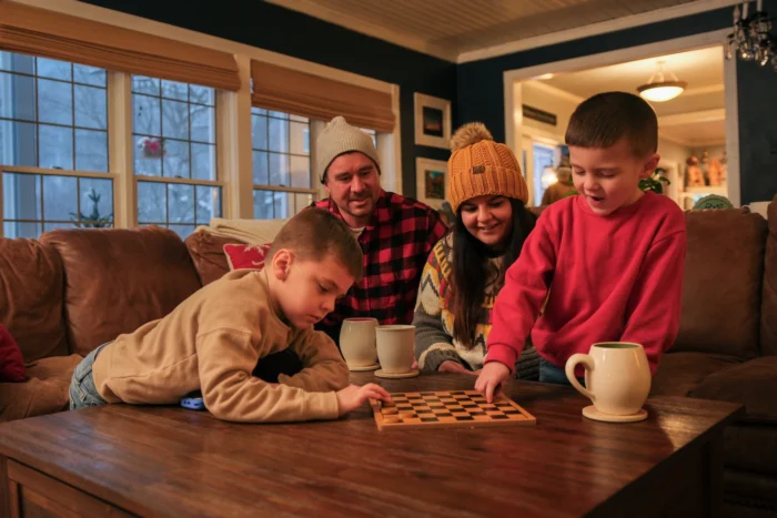 Family of four playing checkers at a table with hot drinks