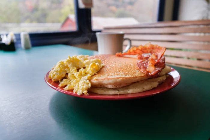 Pancakes, scrambled eggs and bacon on a red plate with a coffee cup in the Station 2 Restaurant.