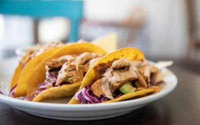 Three chicken tacos with shredded cabbage avocado and sauce on a white plate