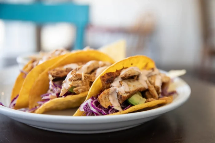 Three chicken tacos with shredded cabbage avocado and sauce on a white plate