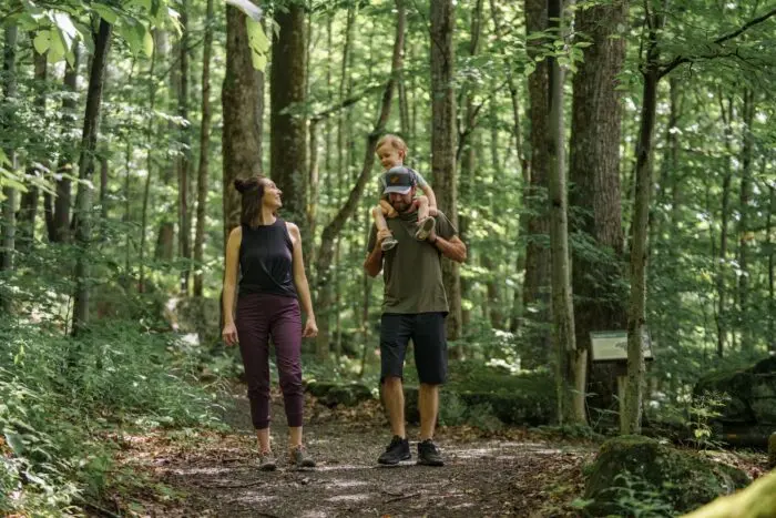 Two adults walk on a forest trail while one carries a child on their shoulders