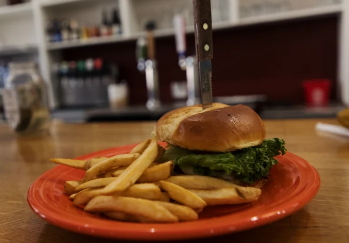 Burger with lettuce on a brioche bun served with fries on a red plate, with a steak knife through the top