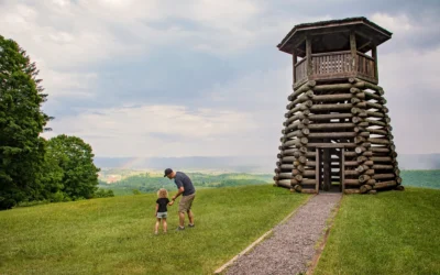 A father and his small child stand beside the lookout tower at Droop Mountain Battlefield State Park, looking out at the green valley below.
