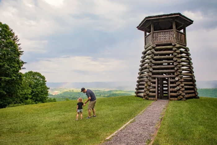 A father and his small child stand beside the lookout tower at Droop Mountain Battlefield State Park, looking out at the green valley below.