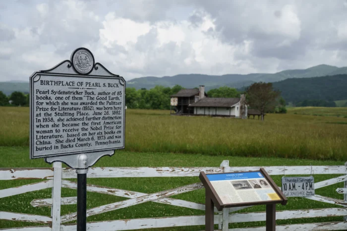 A historical marker designating the birthplace of Pearl S. Buck in a rural landscape with a farmhouse, green fields and mountains in the background.