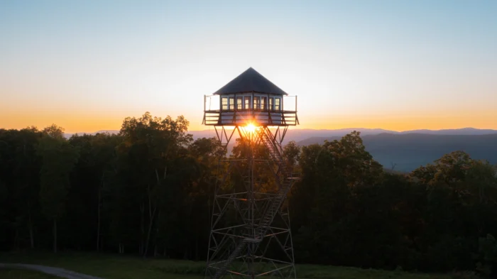 The Thorny Mountain Fire Tower at Seneca State Forest silhouetted against a mountain sunset, sun peeking through its base.