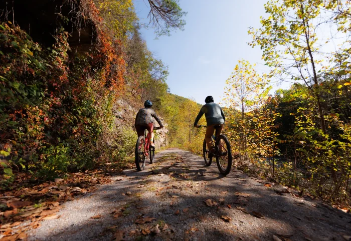 Two people are biking on a gravel path in Pocahontas County. Foliage lines the trail. 